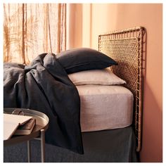 a bed with black sheets and pillows on top of it next to a table in front of a window