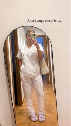 a woman taking a selfie in front of a mirror wearing white scrubs and pink slippers