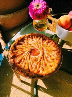 a pie sitting on top of a glass table next to a vase filled with flowers