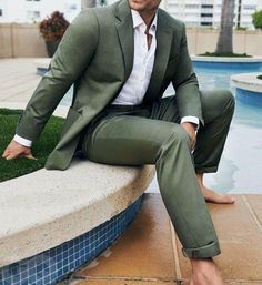 a man in a green suit sitting on a ledge next to a pool with his legs crossed