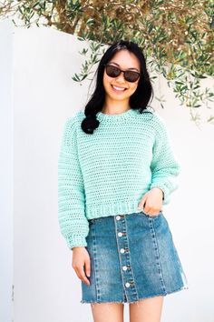 a woman wearing a green sweater and denim skirt standing in front of a white wall