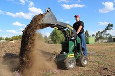 a man standing next to a green tractor in the middle of a field with dirt on it