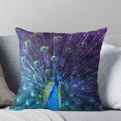 a blue and purple peacock with feathers spread out throw pillow on a white couch cushion