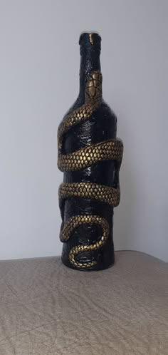 a snake wrapped around a black bottle on a bed with a white wall in the background