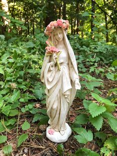 a statue of a woman with flowers on her head in the grass and trees behind it