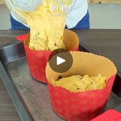 two cupcakes with yellow frosting in red paper cups on a metal tray