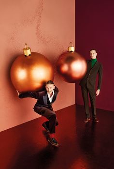 two men in suits are standing next to christmas ornaments on a wall and one man is leaning against the wall