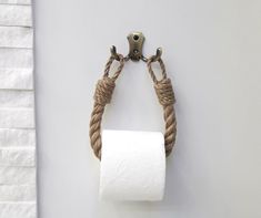 a rope wrapped around a toilet paper roll hanging on a wall next to a metal hook