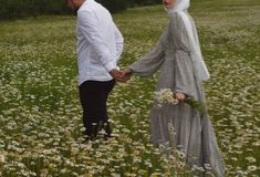 a man and woman holding hands in a field full of flowers