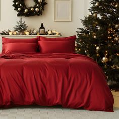 a bed with red sheets and pillows next to a christmas tree