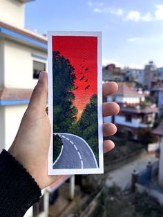 a person holding up a card with an image of a road and trees on it