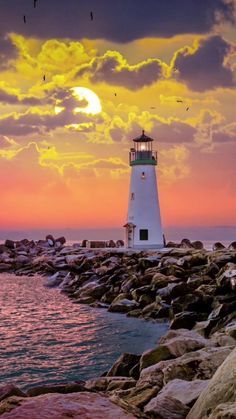 a light house sitting on top of a rocky shore next to the ocean at sunset