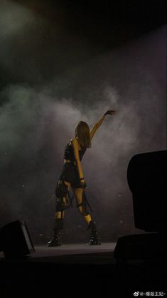 a woman in yellow and black outfit on stage with her arms out to the side