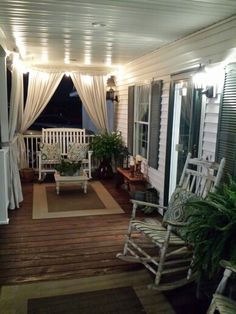 a porch with rocking chairs and curtains on the windowsill is lit up by string lights