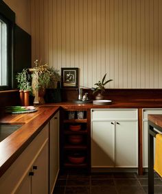 a kitchen with wooden counter tops and white cabinets, along with potted plants in the corner