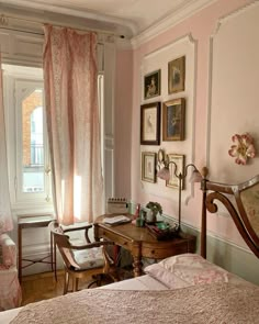 a bedroom with pink walls and pictures on the wall next to a wooden desk in front of a window