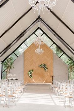 an indoor wedding venue with white chairs and chandelier hanging from the ceiling, surrounded by greenery