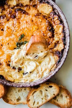 a bowl filled with cheese and crackers on top of a white table next to bread