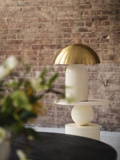 a table lamp sitting on top of a white pedestal in front of a brick wall