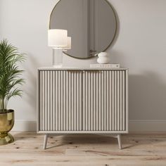 a white cabinet sitting next to a mirror and potted plant on top of a wooden floor