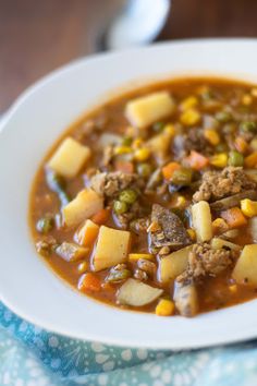 a white bowl filled with meat and vegetable soup on top of a blue table cloth