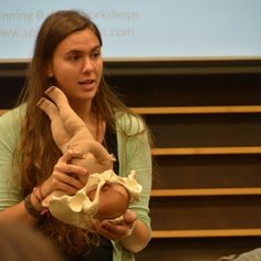 a woman holding a stuffed animal in front of a class room with a projector screen behind her