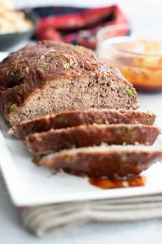 sliced meatloaf on a white plate with sauce and bread in the background, ready to be eaten