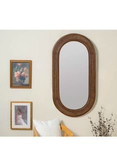 an oval mirror hanging on the wall next to pictures and framed flowers in a vase