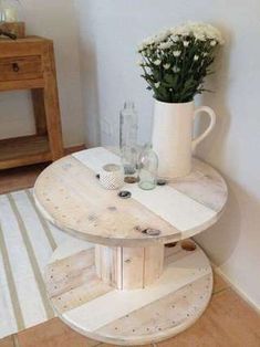 a white vase with flowers sitting on top of a wooden table next to a wall