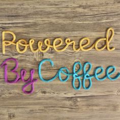 the word powered by coffee written in crochet on a wooden surface with yarn