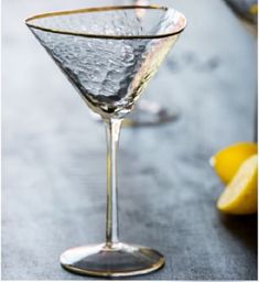 a close up of a martini glass on a table with lemons in the background