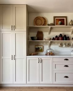 a kitchen with white cupboards and shelves filled with pots, pans and other items