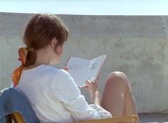 a woman sitting on top of a wooden chair holding a book in her hand and reading it