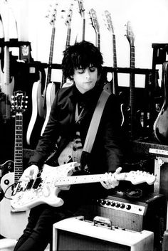 black and white photograph of a man playing an electric guitar in a music store with guitars behind him