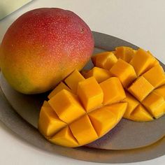 there is a mango on the plate next to it's cut up pieces,