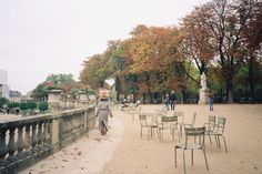 there are many chairs and tables on the sidewalk in this park, with people walking around