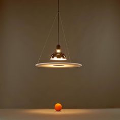 an orange sitting in front of a light hanging from it's side on a table