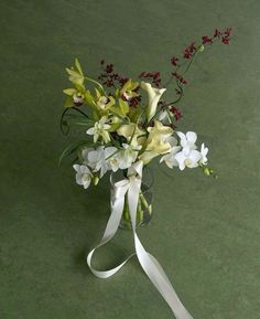 a vase filled with white and green flowers on top of a table next to a ribbon