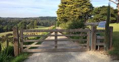 an open wooden gate leading to a lush green field next to a dirt road with trees on both sides