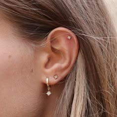 a close up of a woman's ear wearing gold stars and hoops earrings