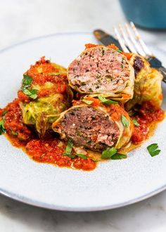 three stuffed cabbages on a white plate with red sauce and a fork next to it