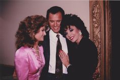 two women and a man standing next to each other in front of a mirror smiling