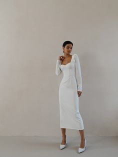 a woman in a white dress is standing against a wall and posing for the camera