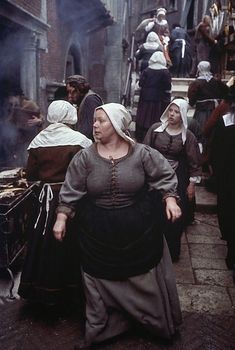 a group of people walking down a street next to each other in historical dress and bonnets