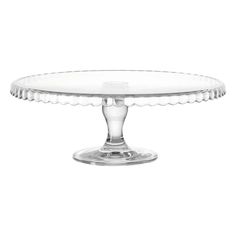 a clear cake plate sitting on top of a white tablecloth covered table with an oval base