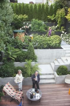 two people are standing on a deck in the middle of an outdoor garden with trees and plants