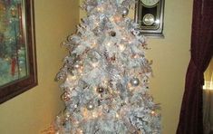 a white christmas tree with silver ornaments in a living room next to a clock on the wall