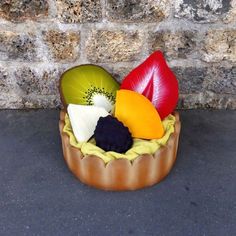 there is a small bowl with fruit in it on the ground next to a brick wall