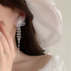 a woman in a white dress is holding her hand up to her face while wearing earrings with flowers on them