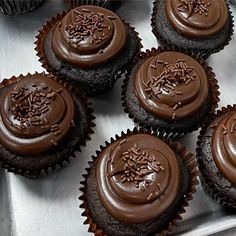 several chocolate cupcakes with frosting and sprinkles on them in a metal tray